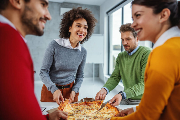 Vzrušená multikulturní skupina podnikatelů, kteří mají k obědu pizzu. - Fotografie, Obrázek
