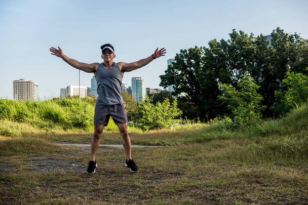 Un atlético asiático hace burpees en un campo abierto cerca de la ciudad. Aptitud cardiovascular. Hacer ejercicio al aire libre. - Foto, imagen