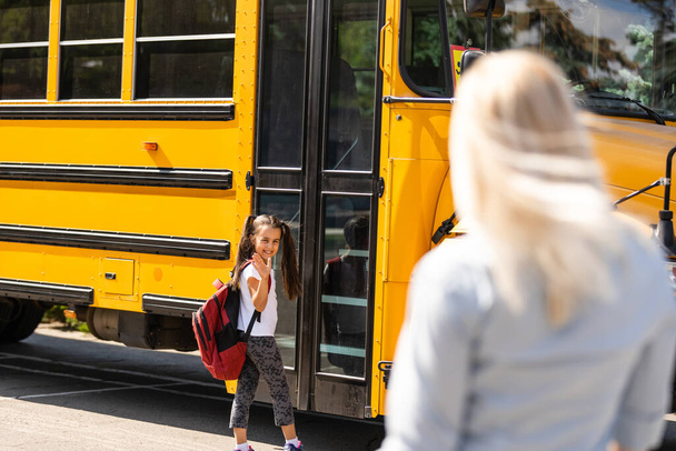 Kids student running into mothers hands to hug her after back to school near the school bus - Photo, Image