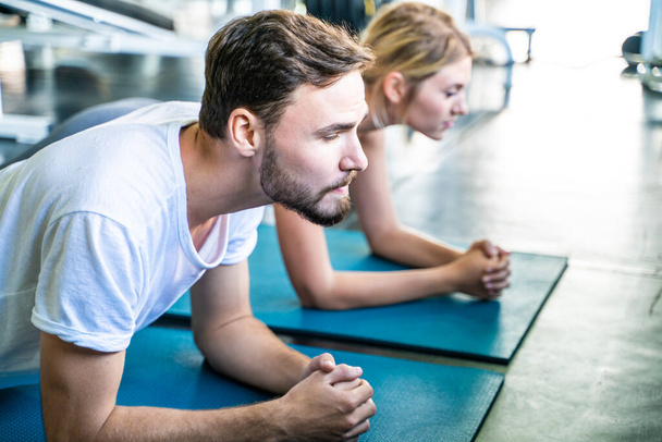Los hombres y las mujeres del deporte ejercitan el tablón en la estera del yoga en el gimnasio del deporte junto edificio del paquete seis - Foto, imagen