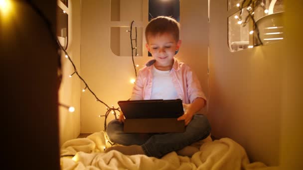 Felice ragazzo allegro sorridente guardare cartoni animati e giochi su tablet computer di notte. Concetto di educazione dei bambini e studio di notte - Filmati, video