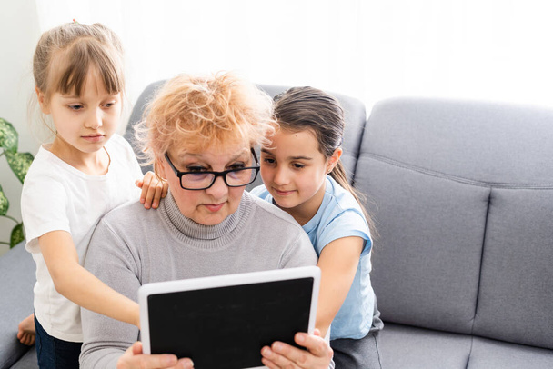 Grootmoeder en twee kleindochters gebruiken thuis een tablet - Foto, afbeelding