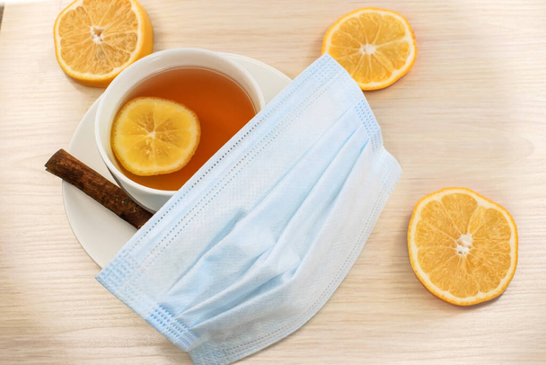 Medical concept. Medical face mask on a cup of lemon tea. Lemon slices and a wooden table. - Foto, afbeelding