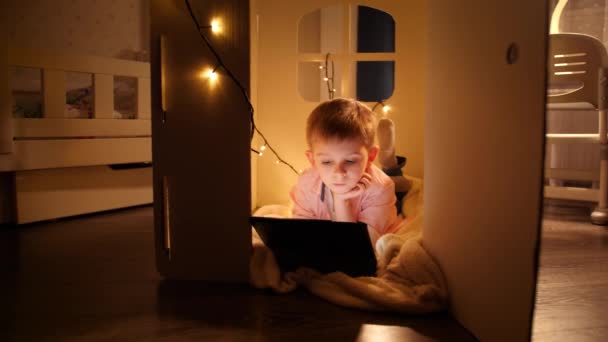 Panning laukaus pieni fiksu poika makaa pieni lelutalo ja uing tabletti tietokone yöllä. Lastenkasvatuksen ja opiskelun käsite yöllä - Materiaali, video