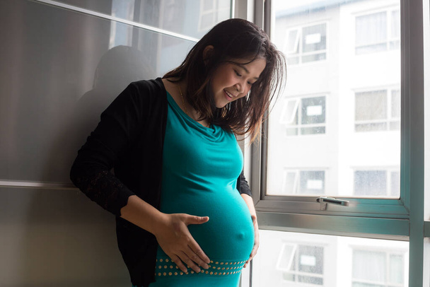 Terhes nők hasa áll ablak mellett függöny a szobában - Fotó, kép