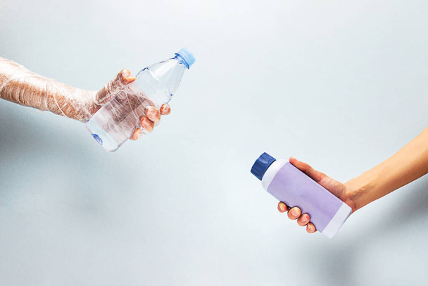 Uma garrafa de água de plástico na mão envolta em polietileno e uma garrafa de água reutilizável na outra mão. Nenhum conceito de plástico. - Foto, Imagem