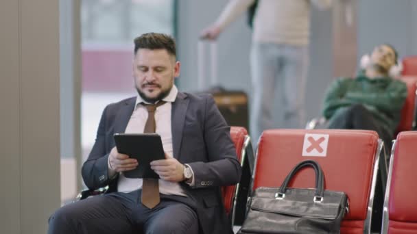 Středně zpomalené záběry úspěšného podnikatele s digitálním tabletem na služební cestě čekajícího na let v odletové hale - Záběry, video