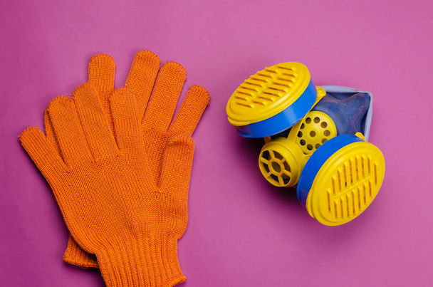 Sarı ve mavi solunum cihazı ve pembe arka planda koruyucu eldivenler. Gazlara (toz, duman, sis) veya zararlı gazlara karşı özel bir kişisel solunum koruma aracıdır. Seçici odak. - Fotoğraf, Görsel