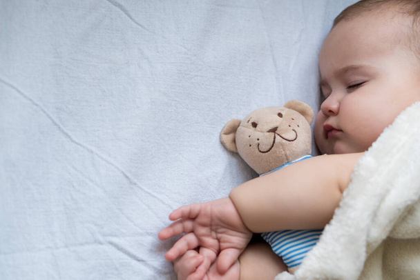Детство, уход, материнство, концепции здоровья - Закрыть Маленький мир тихий младенец малышка спит ребенок спит глубокий сон положить обнять плюшевого медведя игрушку на мягкое теплое одеяло с закрытыми глазами на большую кровать - Фото, изображение