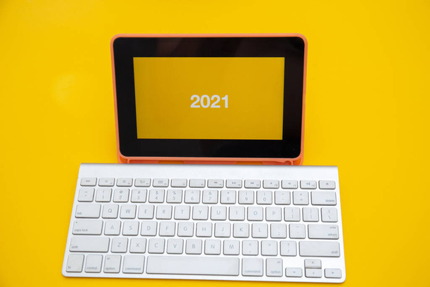 黄色の背景に隔離されたワイヤレスキーボードとデジタルタブレット画面上の2021テキスト - 写真・画像