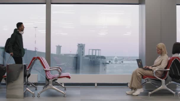 Imágenes retrospectivas de cámara lenta completa del hombre con el equipaje parado junto a la ventana mirando la pista de aterrizaje esperando el vuelo en la sala de salida - Metraje, vídeo