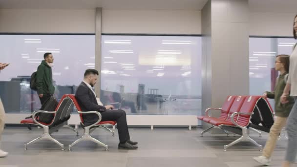 Slow-motion steekbeelden van passagiers die heen en weer lopen op de wachtruimte van de luchthaven en zakenman die aan de laptop werkt voordat ze instappen - Video