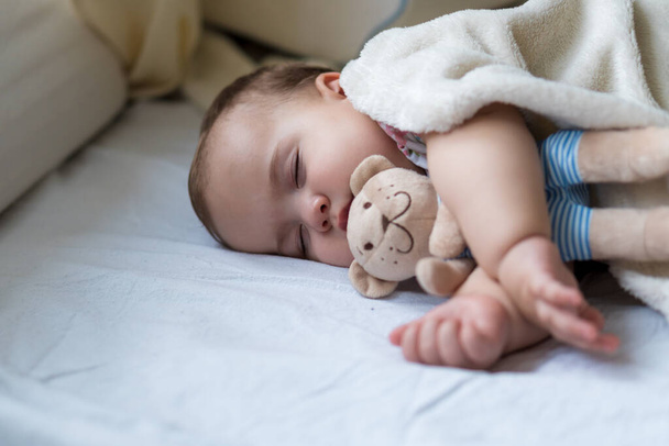 Childhood, care, motherhood, health concepts - Close up Little peace calm infant toddler baby girl sleep resting take deep nap laying hug teddy bear toy on soft warm blanket with close eyes on big bed - 写真・画像