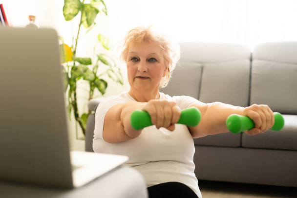 Exercice de femme âgée utilisant des instructions en ligne ordinateur portable aux soins de santé à domicile - Photo, image