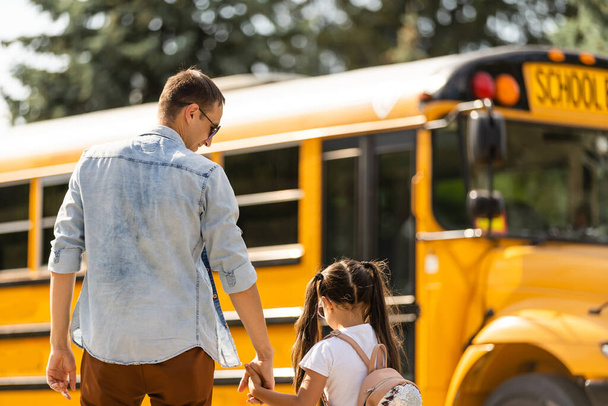 Κορίτσι με τον πατέρα πηγαίνει πίσω στο σχολείο κοντά στο σχολικό λεωφορείο - Φωτογραφία, εικόνα
