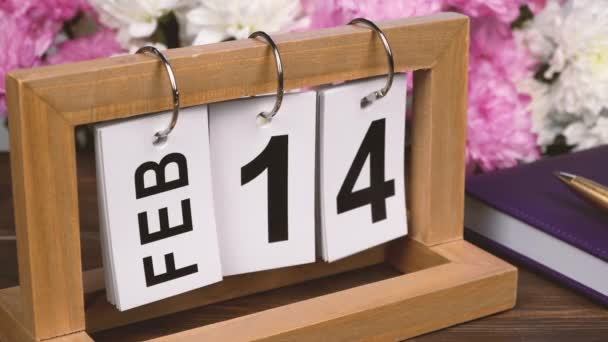 Kalendarz pulpitu z datą 14 lutego i bukiet pięknych kwiatów. Delikatne chryzantemy na Walentynki. Ręcznie robiony kalendarz drewna z datą miesiąca i dnia. planowanie na dzień. - Materiał filmowy, wideo