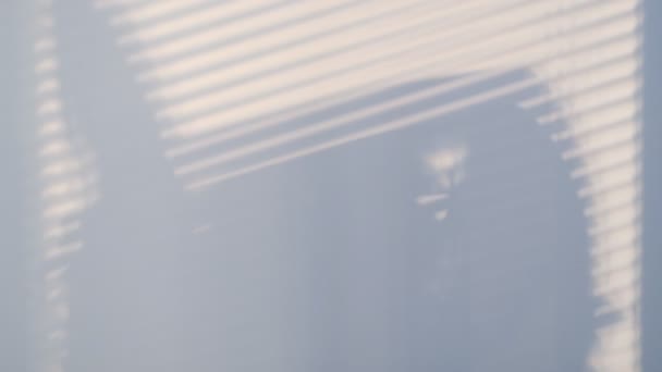 Schatten an der Wand aus einem Fenster mit Jalousien und einer Frauensilhouette. Verschwommene dunkle Schatten, die sich an der Wand bewegen. Schattenbewegung. Zeitlupenvideo. Archivbild - Filmmaterial, Video
