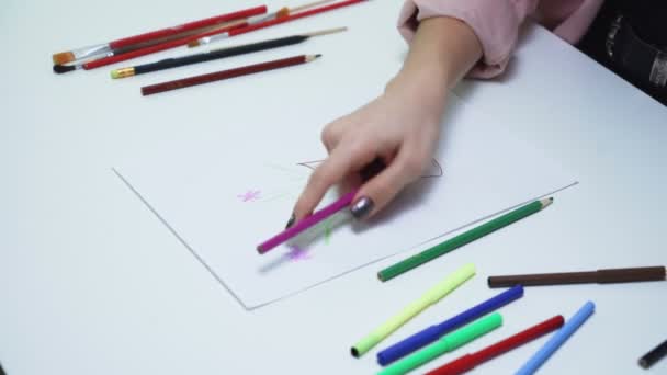 Aantrekkelijke jonge vrouw gebruikt gekleurde potloden om een tekening te maken op een wit papier aan tafel - Video
