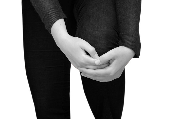 A woman holds on to a sore knee. Horizontal, black and white isolated photo. - Valokuva, kuva