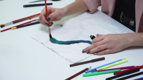 Houkutteleva nuori nainen piirtää vihreällä akryylimaalilla valkoisella liinalla pöydässä - Materiaali, video