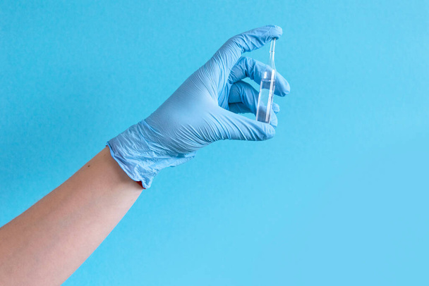 Hand in protective blue gloves hold medicine bottle of vaccine on blue background. Concept of vaccination and healthcare. Space for text - Foto, imagen