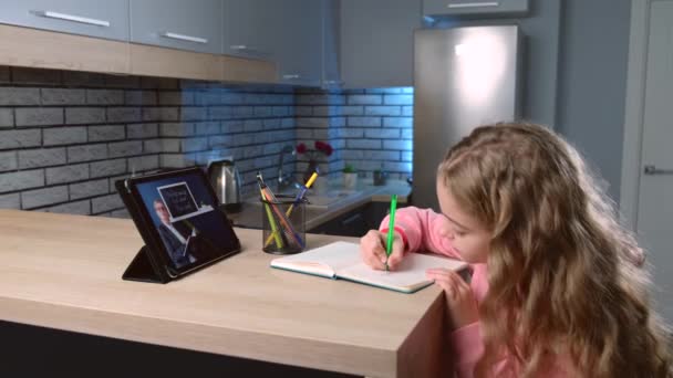 Petite fille caucasienne écoute l'enseignant tout en expliquant le sujet sur une tablette numérique de la maison et écrire des notes dans le copybook - Séquence, vidéo