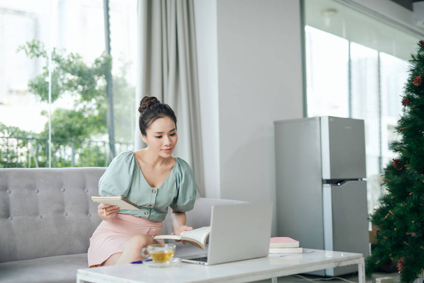 Mujer pensativa usando el ordenador portátil, mirando a un lado mientras está sentado en un sofá acogedor. Madura femenina pensando en un nuevo proyecto de trabajo - Foto, Imagen