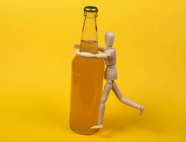 Alcoholism. Wooden puppet and bottle of beer on yellow background. - Fotó, kép