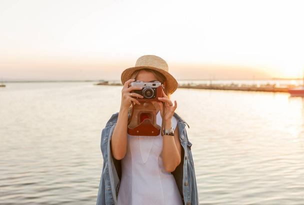 Jonge vrouw maakt een foto op camera bij zonsopgang op zee. Reizen en toerisme - Foto, afbeelding