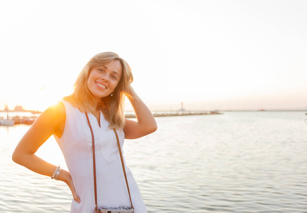 Veselá a veselá atraktivní blondýnka při východu slunce na pláži. Koncept cestování a volného času - Fotografie, Obrázek