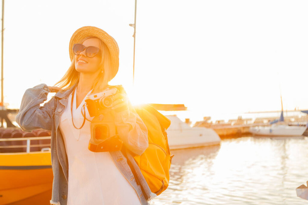 Young woman tourist with large travel backpack and camera at sunrise at yacht Club. Travel and tourism concept - Foto, imagen