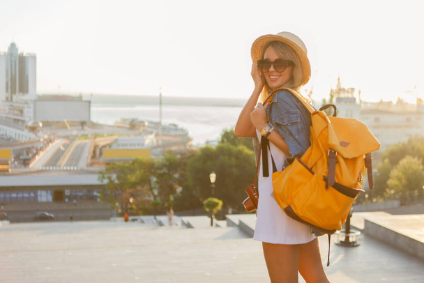 Gün doğumunda şehirde büyük bir sırt çantasıyla gülümseyen genç kadın turistin portresi. Seyahat kavramı - Fotoğraf, Görsel