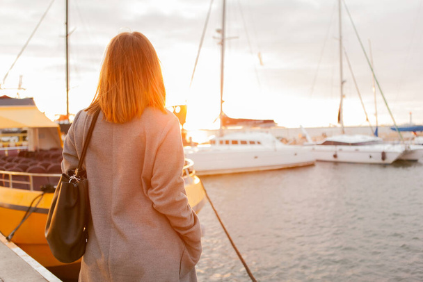 Kobieta w jesiennym płaszczu pozuje w klubie jachtowym o wschodzie słońca - Zdjęcie, obraz