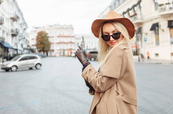 Retrato de jovem mulher loira elegante no casaco de outono, óculos de sol e chapéu de feltro usar luvas na cidade europeia. Menina bonita atraente - Foto, Imagem