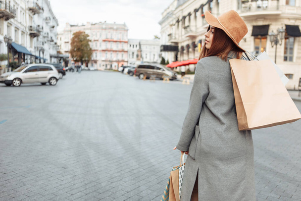 Cute attractive shopaholic funny woman in autumn coat and hat holding many paper shopping bags iin European city - Φωτογραφία, εικόνα