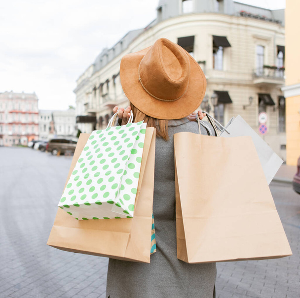 Nette attraktive Shopaholic Frau in Herbstmantel und Hut hält viele Papiereinkaufstüten in der europäischen Stadt - Foto, Bild