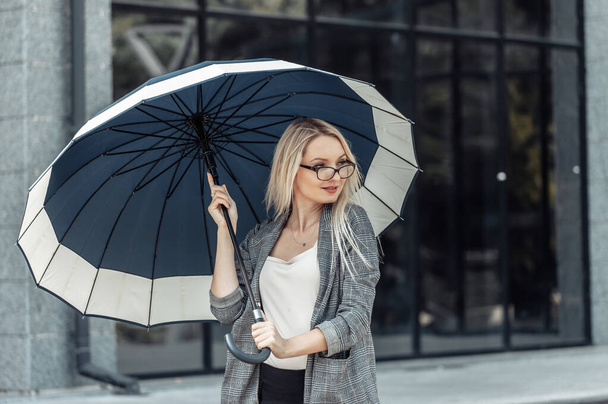 Mujer rubia de negocios con paraguas en el fondo de una oficina de negocios. Esperando la lluvia - Foto, Imagen