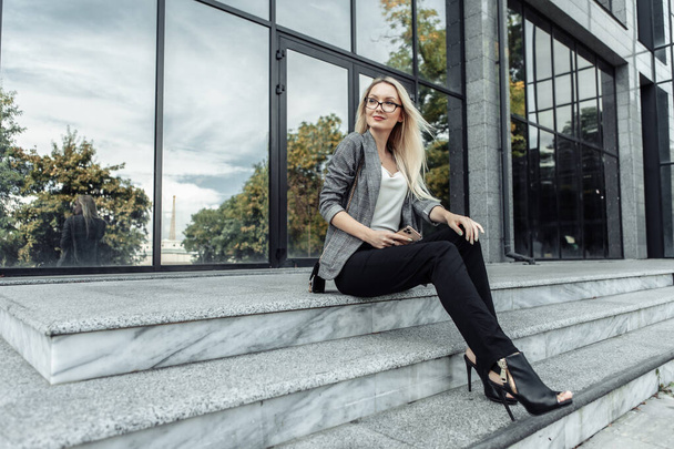 Happy Business woman sitting on the steps during the break on the background of a business center - 写真・画像