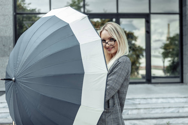 Счастливая деловая женщина открыла зонтик на фоне делового офиса. В ожидании дождя - Фото, изображение