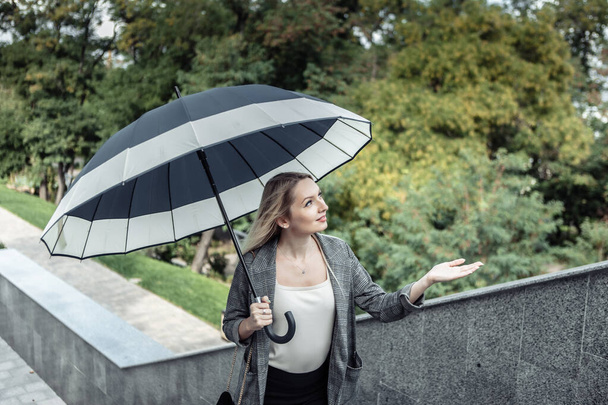 Білявка Бізнес-леді тримає парасольку і перевіряє дощ, піднімаючись по сходах на відкритому повітрі
 - Фото, зображення