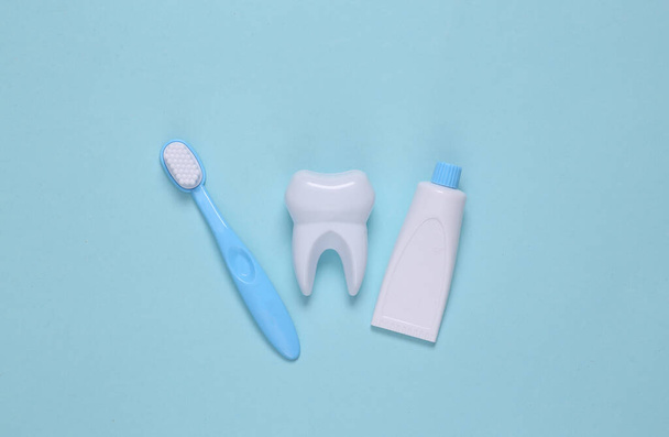 Diente falso, cepillo de dientes y pasta de dientes sobre fondo azul. Vista superior - Foto, imagen
