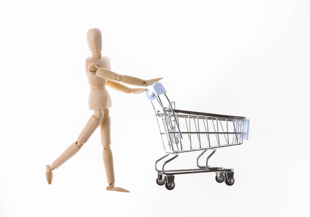 Shopping concept. Wooden puppet with supermarket trolley isolated on white background - Φωτογραφία, εικόνα