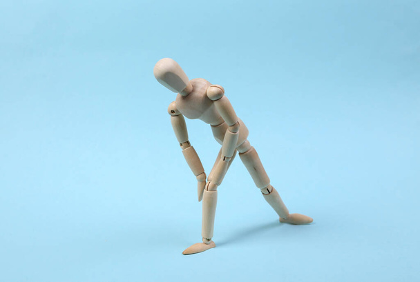 Drewniana marionetka ranna z bólem nóg na niebieskim tle - Zdjęcie, obraz