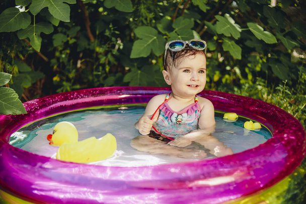 Színes portré vidám baba élvezi a napot a kis medencében, és a kezében a napszemüveg - Fotó, kép