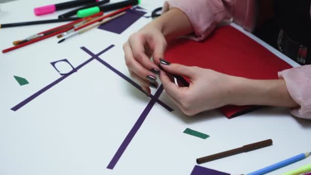 Bovenaanzicht van de vrouw maakt een ambacht van een paars papier en lijm aan de tafel in een witte studio - Video