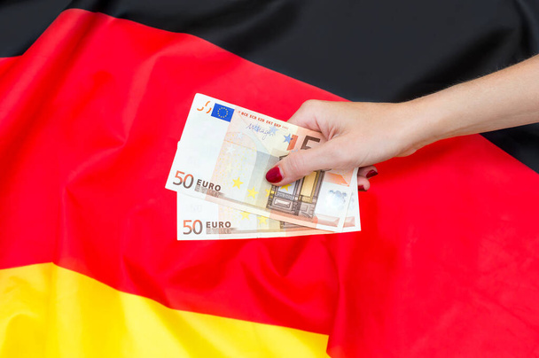 Γυναικείο χέρι που κρατά χαρτονομίσματα του ευρώ κατά της γερμανικής σημαίας. - Φωτογραφία, εικόνα