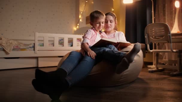 ベッドに行く前におとぎ話の本を読んで母親と小さな男の子のドリーショット。夜間に一緒に時間を持つ子供の教育と家族の概念 - 映像、動画