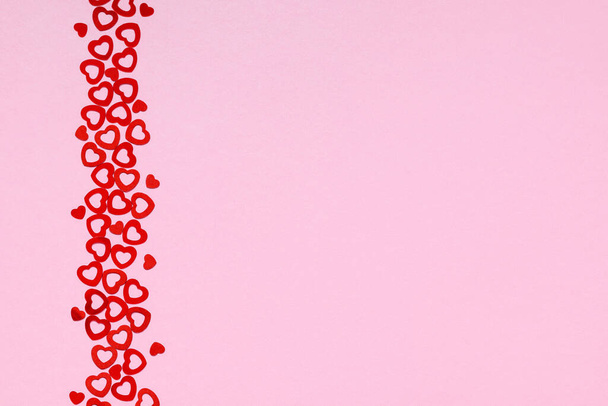 Vista dall'alto della striscia verticale di piccoli coriandoli a forma di cuore su sfondo rosa, copiare spazio. San Valentino sfondo. - Foto, immagini