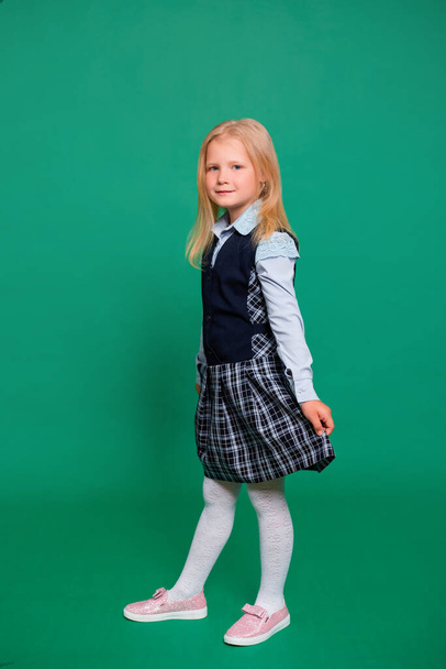 Young girl in school uniform posing on a green background. - Foto, imagen