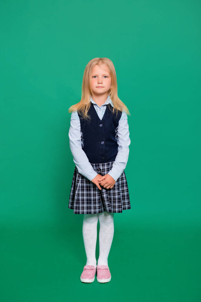 Young girl in school uniform posing on a green background. - Φωτογραφία, εικόνα